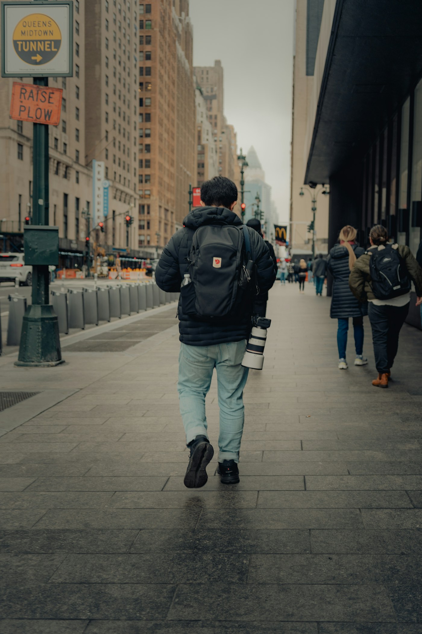 A photographer with a backpack and camera walking along a city street