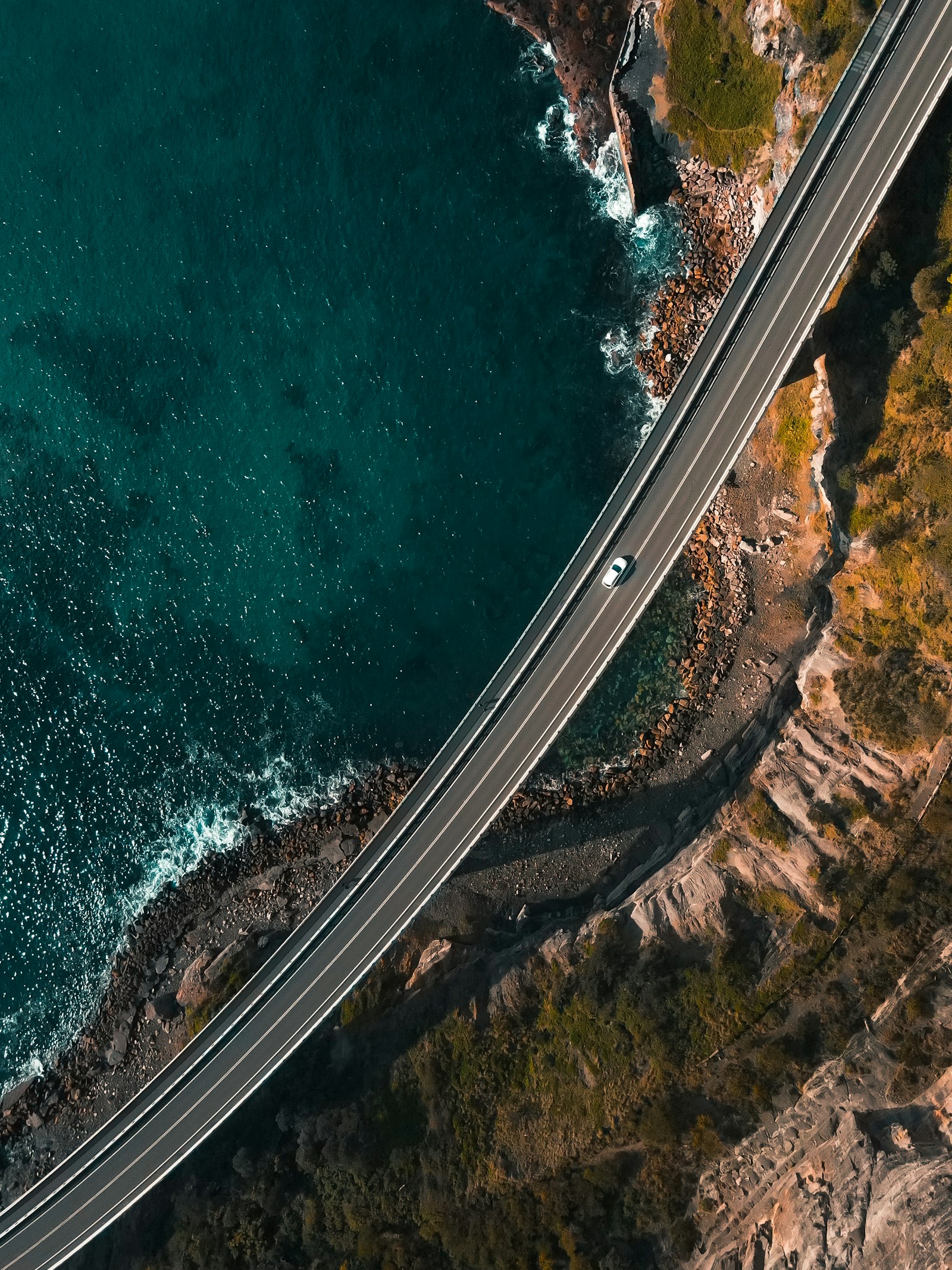 An aerial view of a road curving beside vivid turquoise ocean water