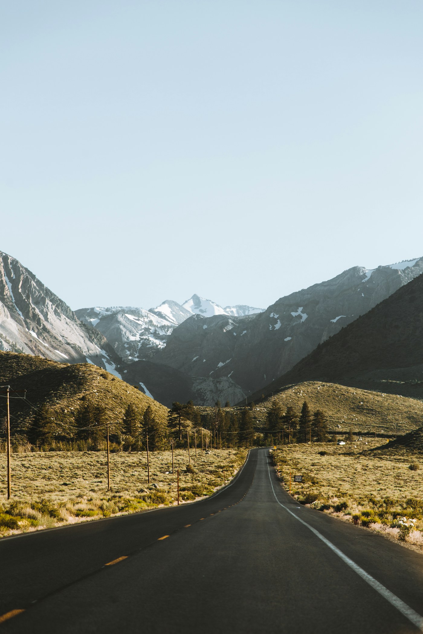 A highway running through a dry valley toward snow-dusted mountain peaks