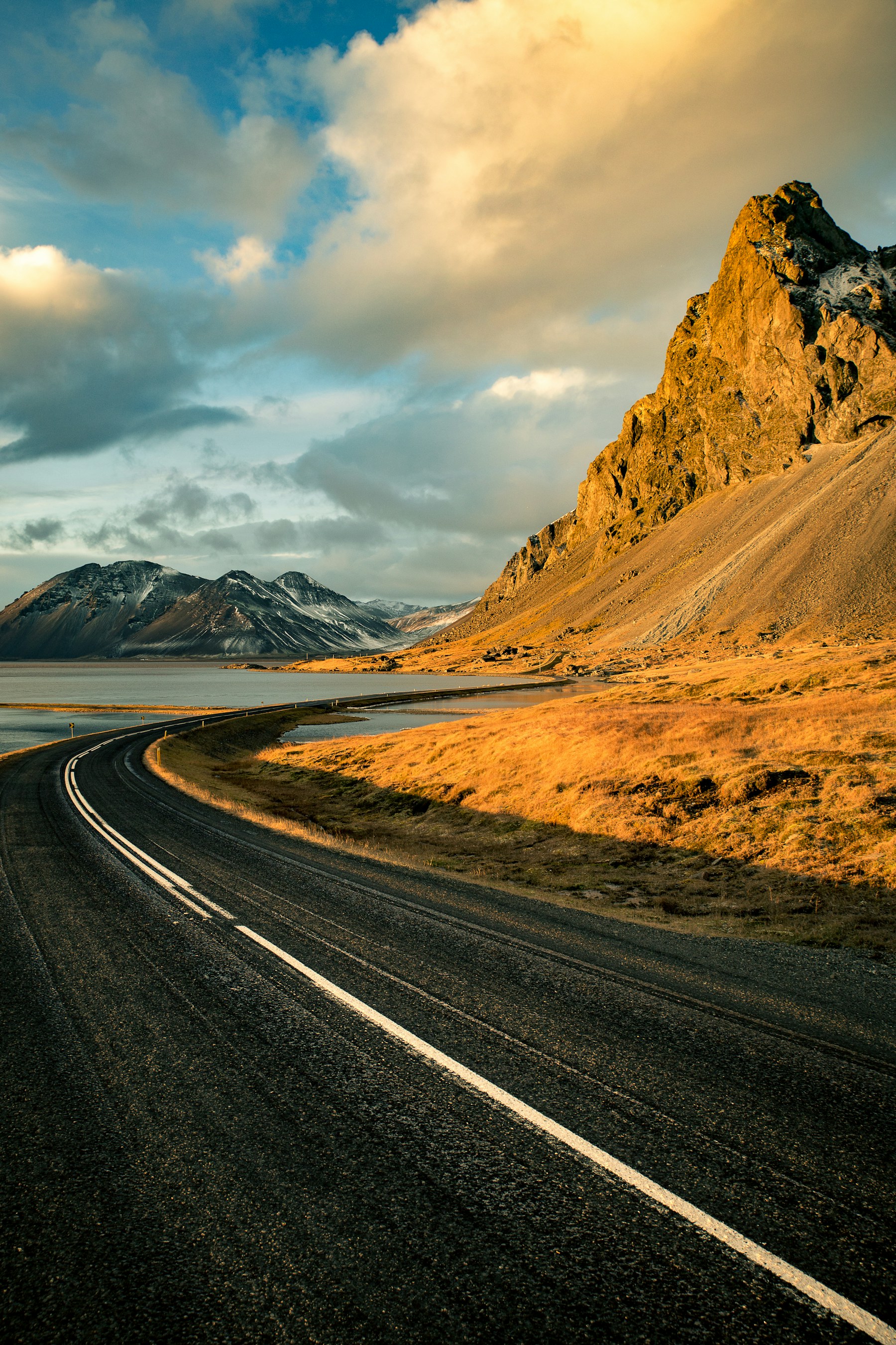 A winding road crossing a golden valley toward distant mountains at sunset