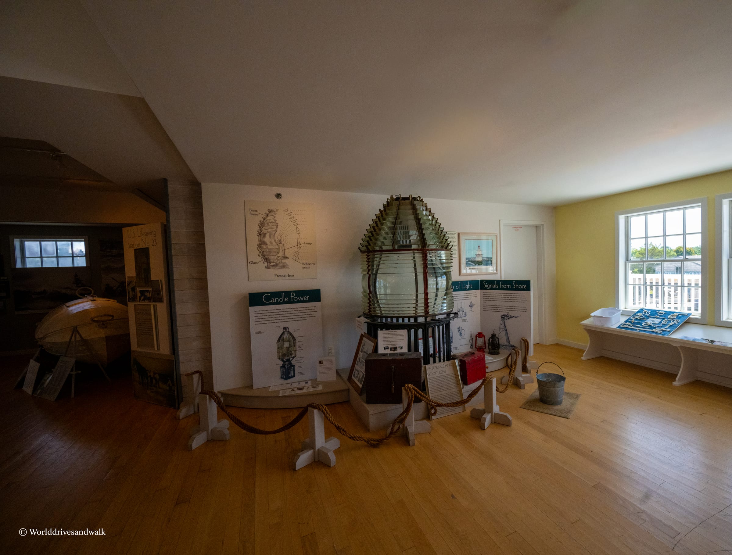 An interior view of the Tucker Island Light House Museum in New Jersey, featuring a large glass lantern, informational displays, and a wooden floor.